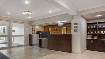 A reception area with a reception desk, a computer, and a wooden wall with artwork. There are signs indicating check-in and check-out times.