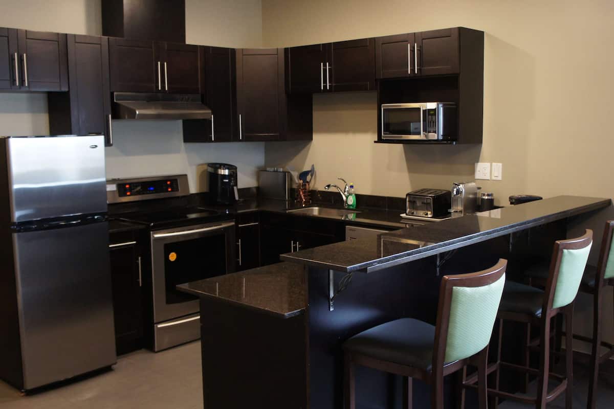 A modern kitchen with dark cabinetry, stainless steel appliances, and a bar area with bar stools.