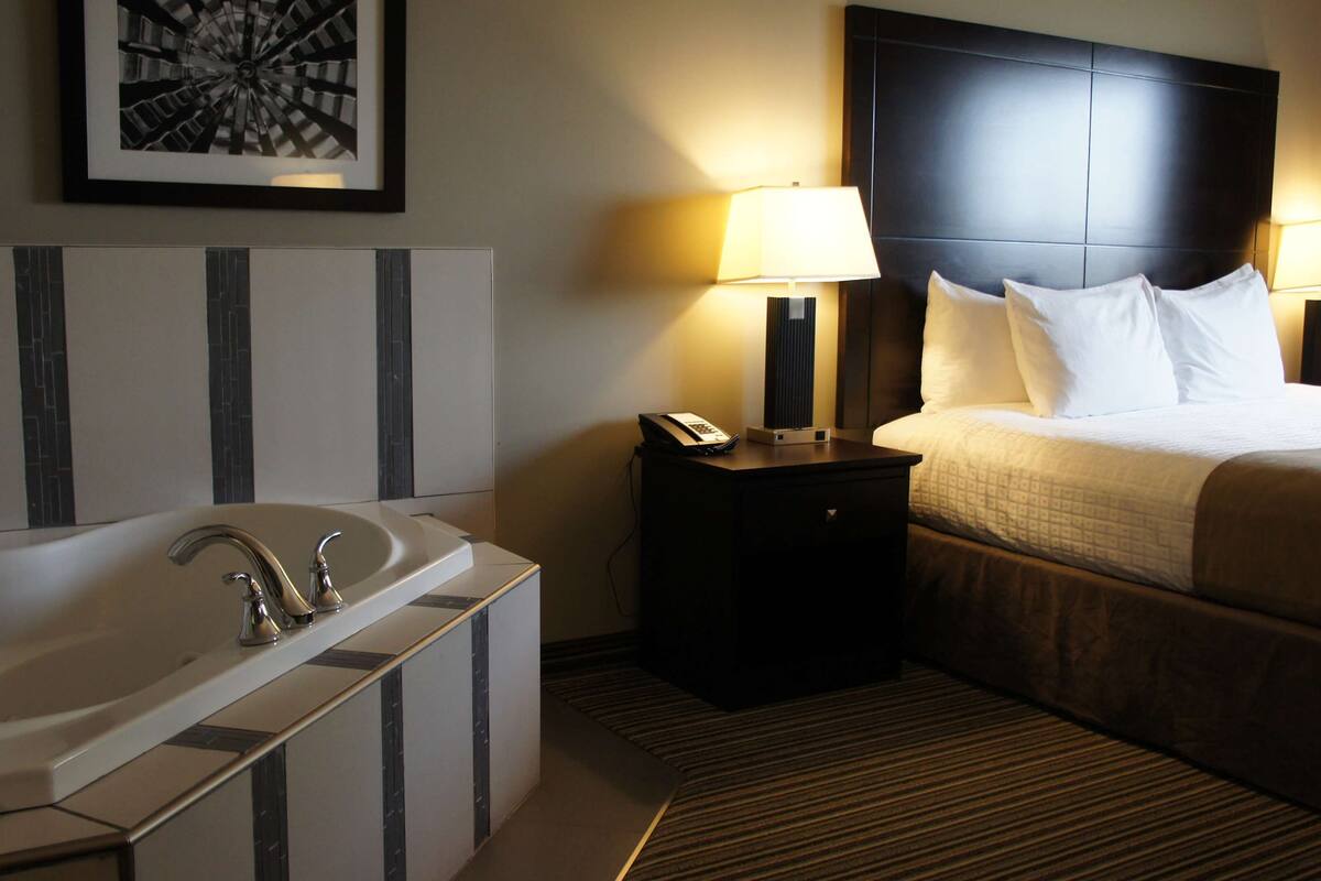 A hotel room with a large bed, two bedside lamps, a telephone, and a bathtub.