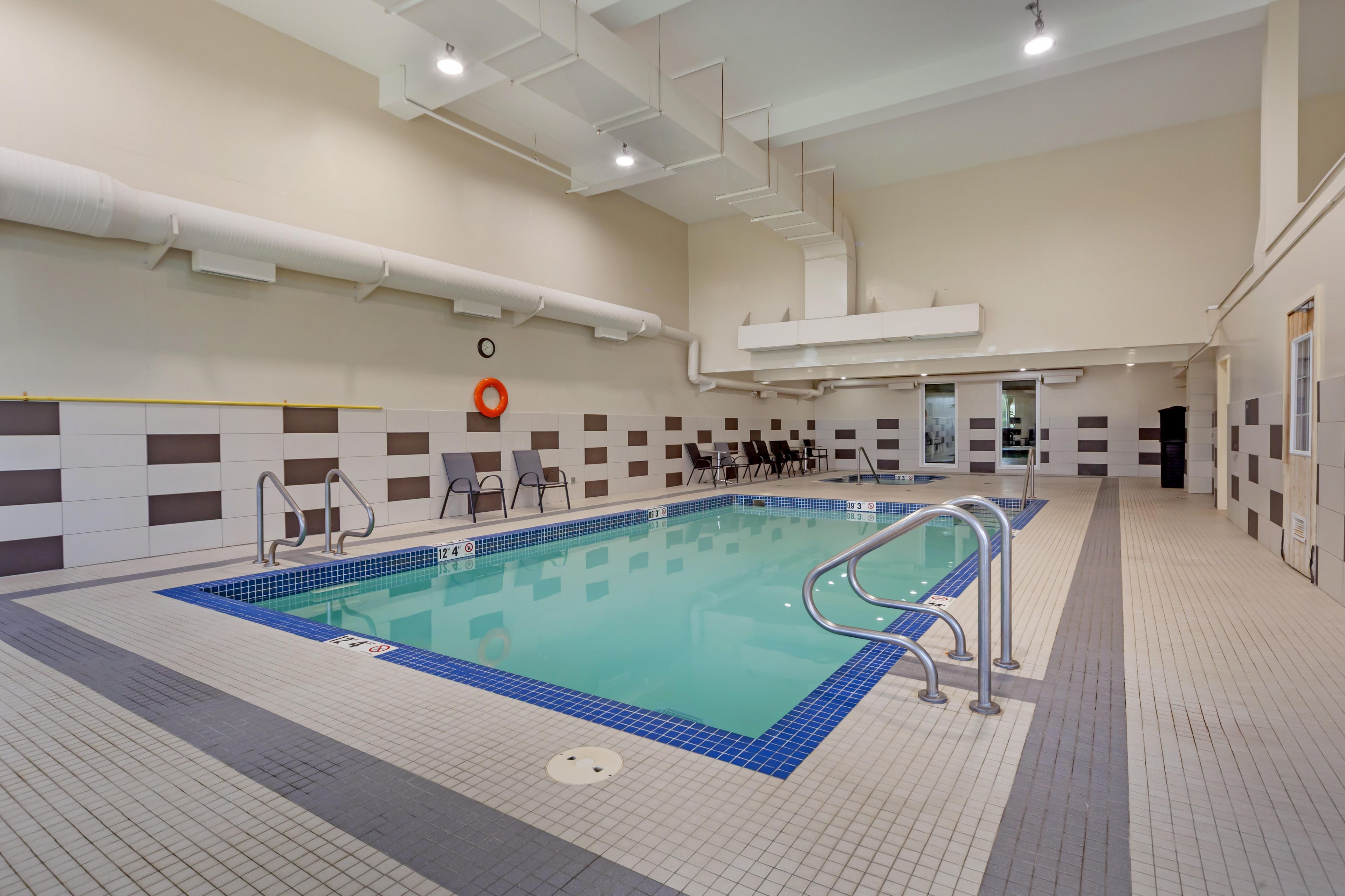 Una piscina con cubierta de azulejos, una silla salvavidas y un cartel de seguridad.