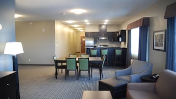 A hotel room with a dining area, kitchenette, and seating.