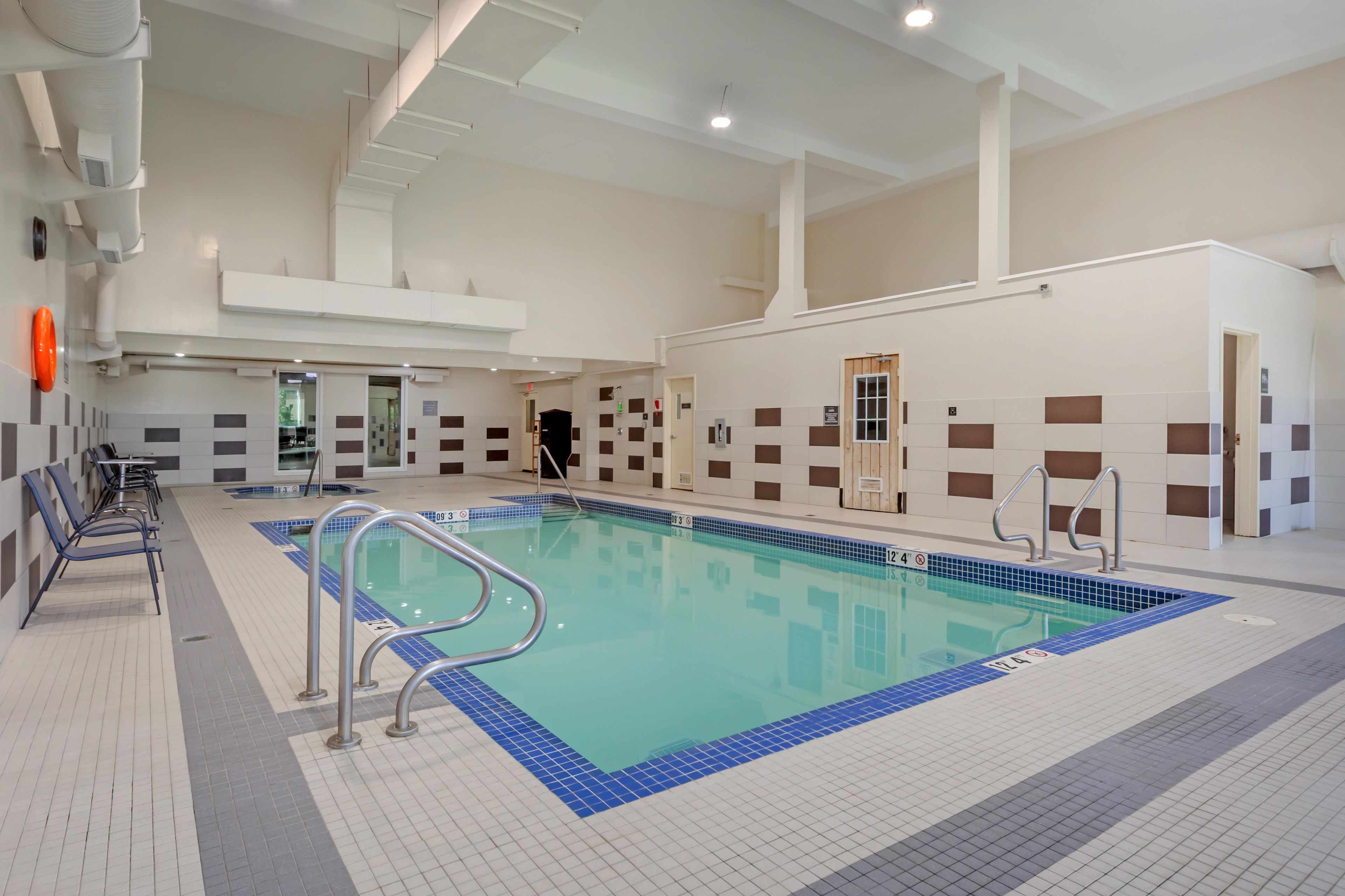 An indoor swimming pool with clear lane markings, a poolside seating area, and a tiled wall with a checkered pattern.