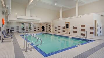 An indoor swimming pool with clear lane markings, a poolside seating area, and a tiled wall with a checkered pattern.