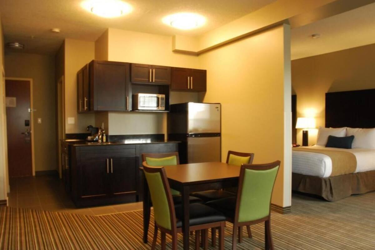 A hotel room with a kitchenette, a dining area with a table and chairs, and a bed with a headboard.