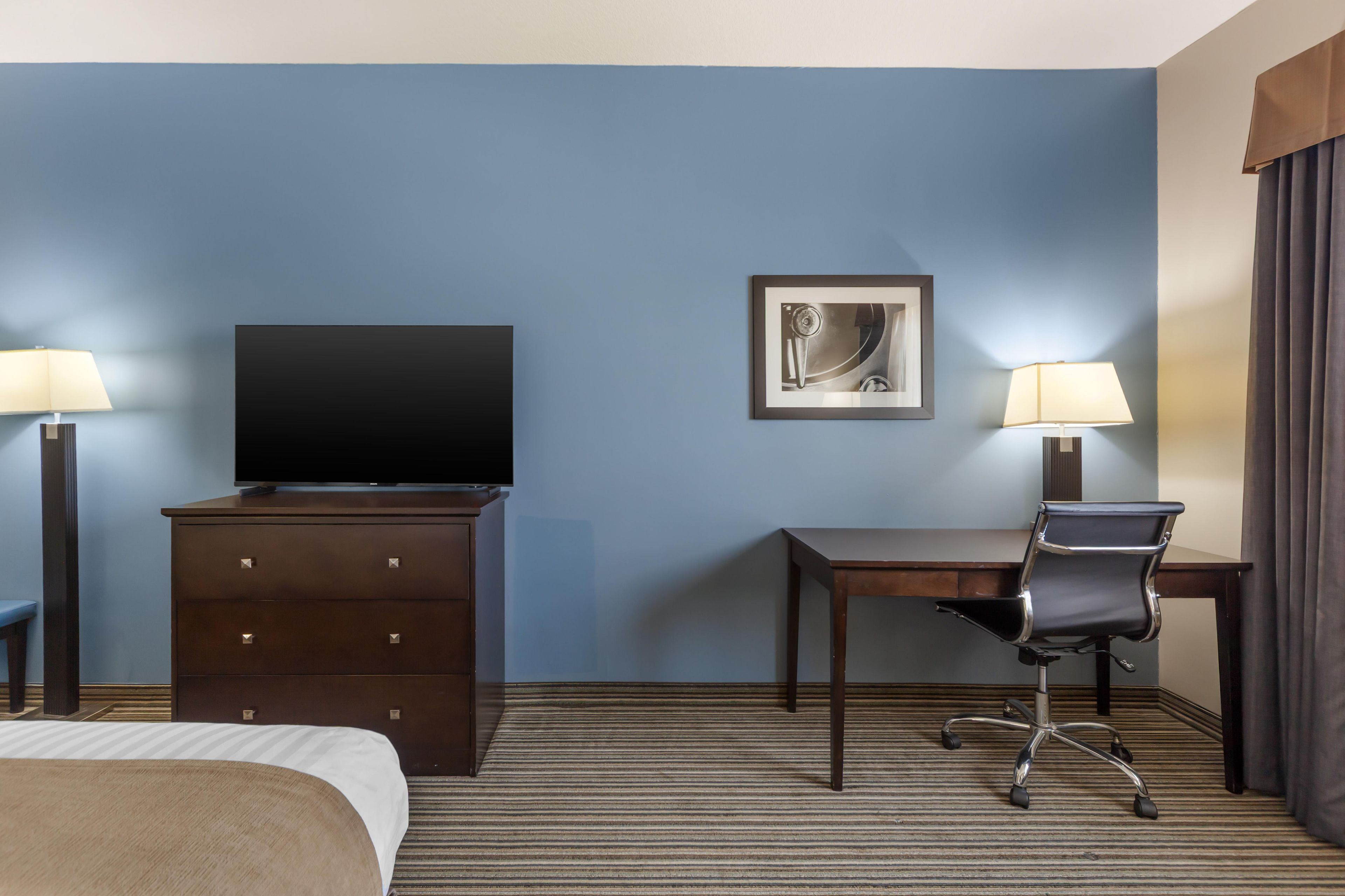 A hotel room with a bed, a desk, a chair, a television, and two lamps.