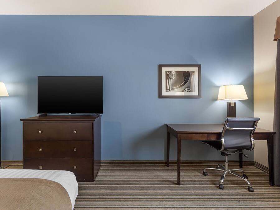A hotel room with a bed, a desk, a chair, a television, and two lamps.