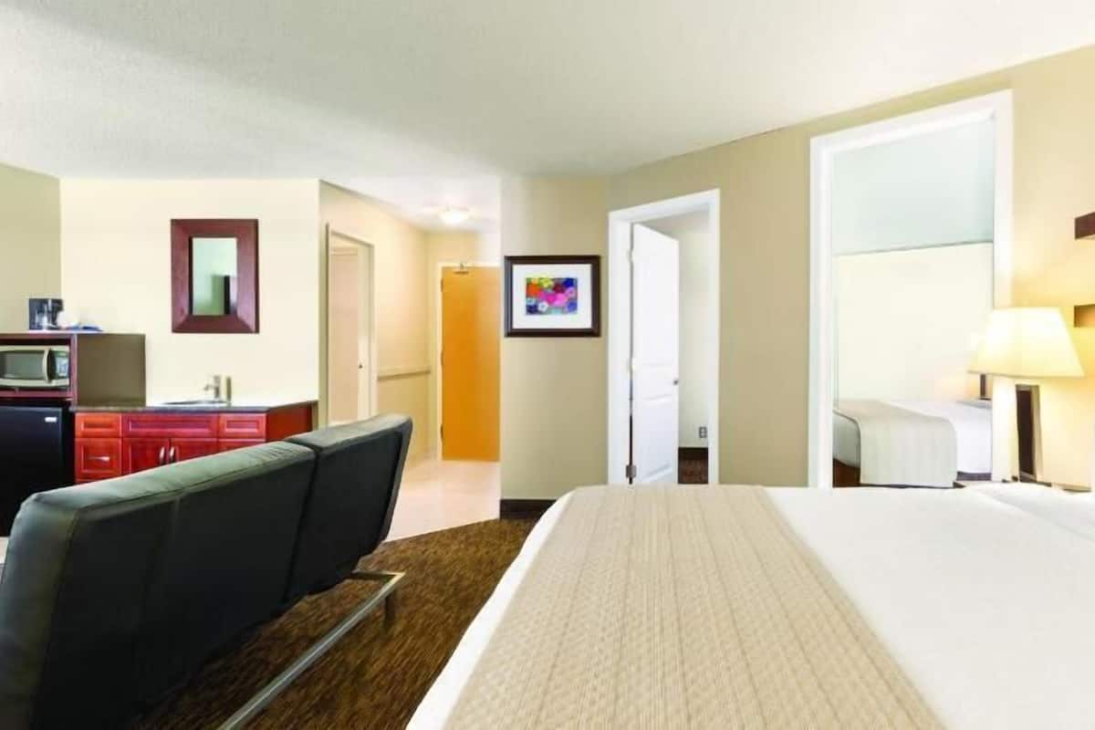 A hotel room with a large bed, a desk with a chair, a television, and a door leading to another room.