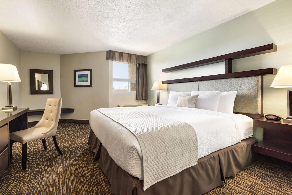 A hotel room with a large bed, a desk, a chair, and a window.
