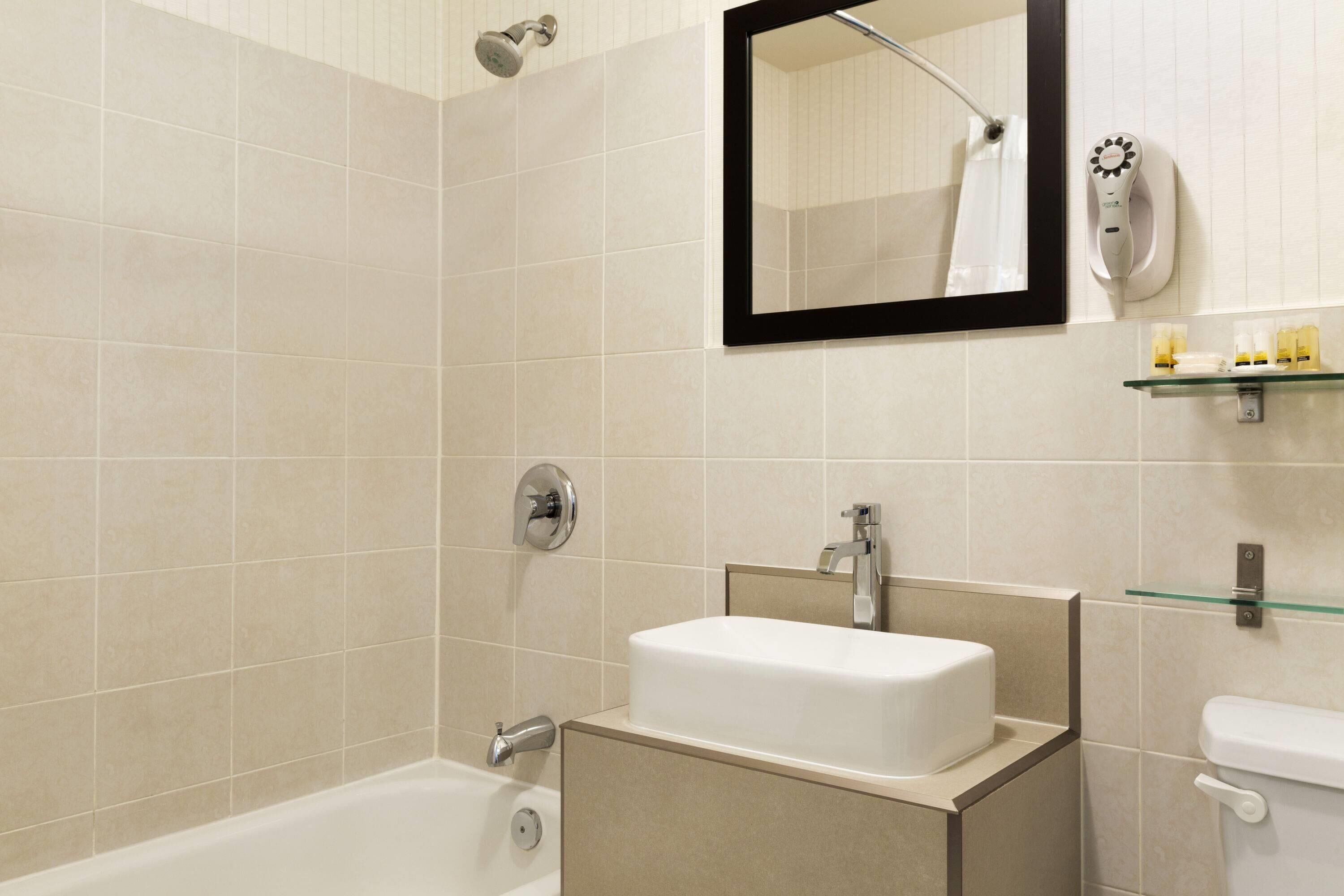 Un baño moderno con bañera, lavamanos, espejo y secador de pelo montado en la pared.