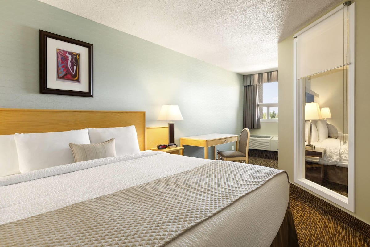 A hotel room with a large bed, a desk, a chair, a window, and a framed picture on the wall.