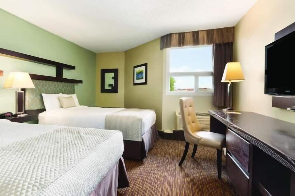 A hotel room with two beds, a desk, a chair, a television, and a window.