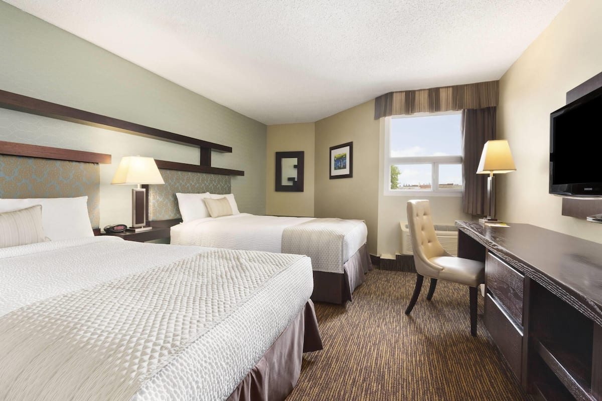 A hotel room with two beds, a desk, a chair, a TV, and a window.