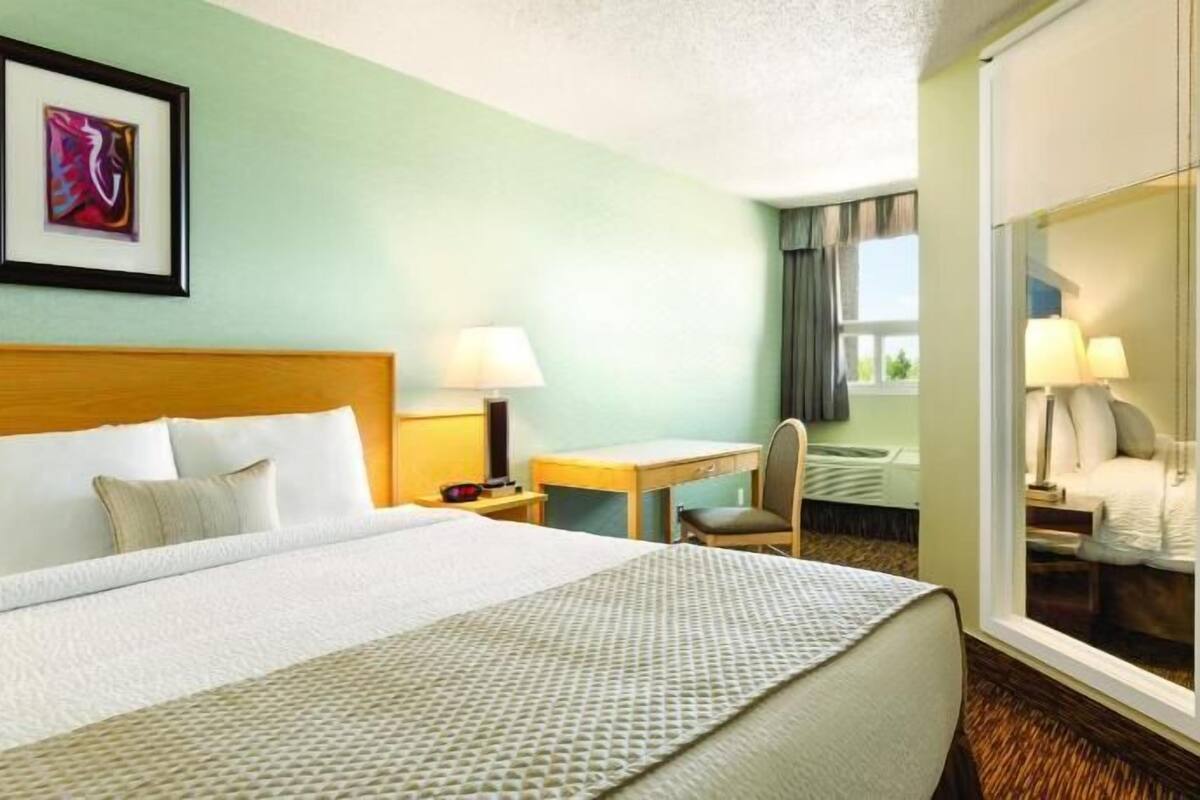 A hotel room with a bed, a desk, a chair, a mirror, and a picture on the wall.