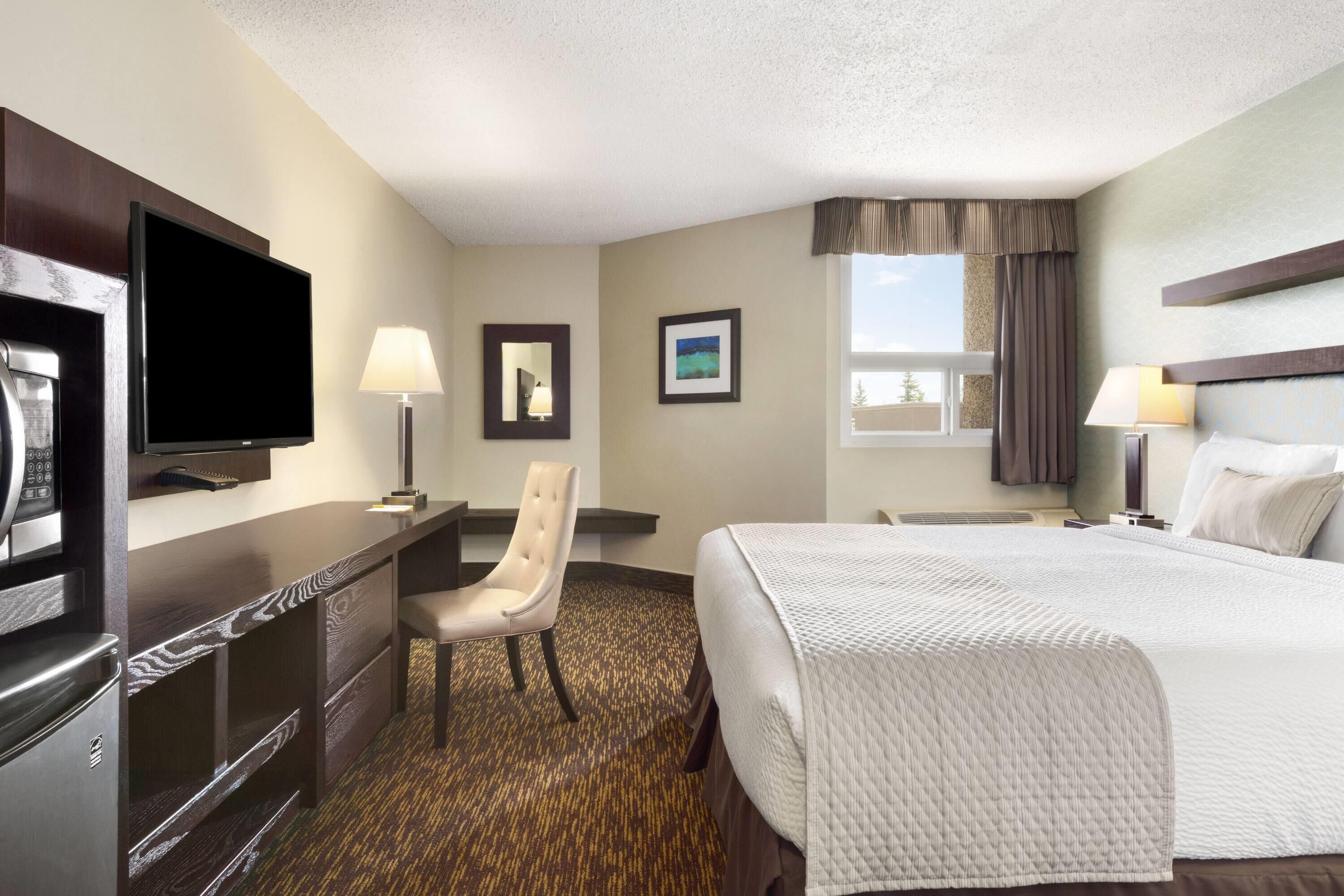 A hotel room with a bed, a desk, a chair, a television, and a window with curtains.