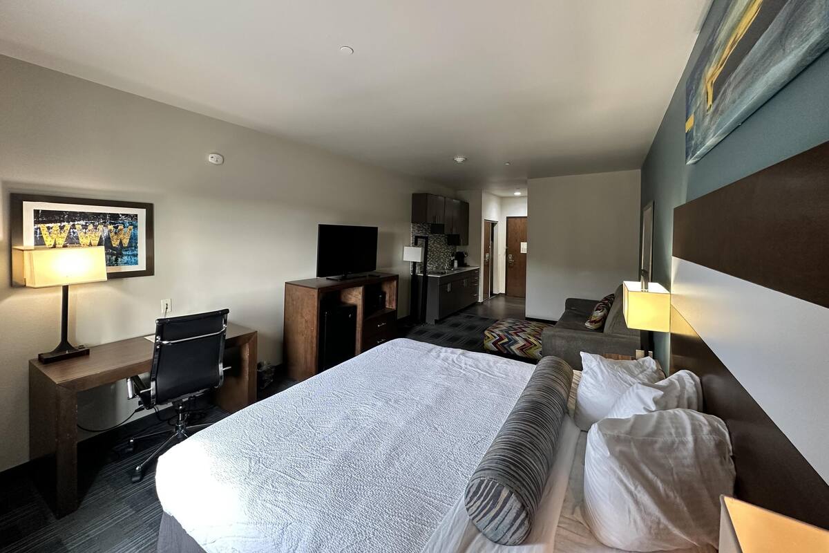 A hotel room with a large bed, a desk with a computer, a television, and a kitchenette.