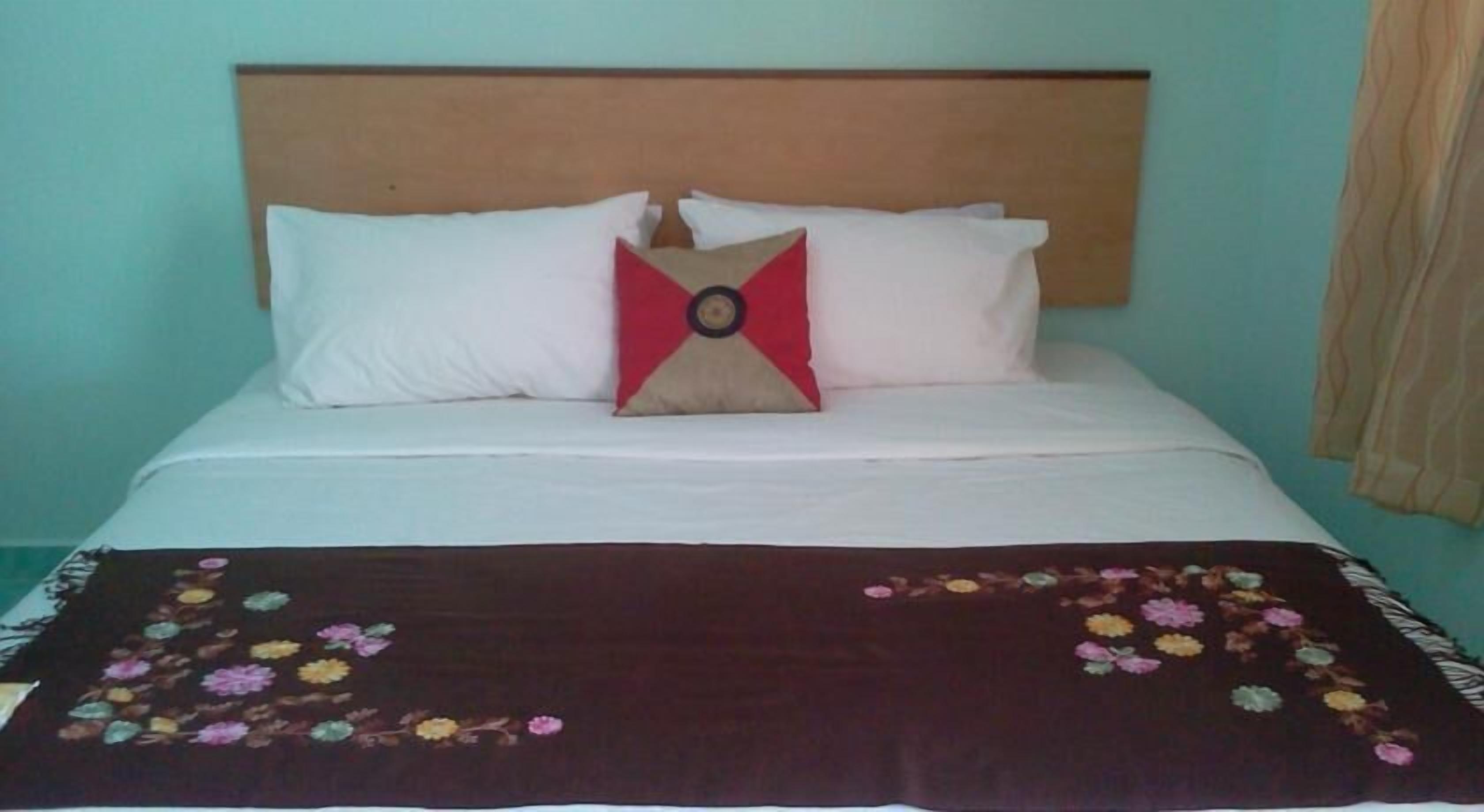 A bed with a wooden headboard, white pillows, and a red and beige pillow. A floral-patterned blanket is on the bed.