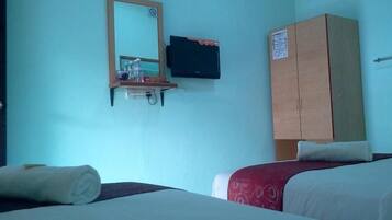 A hotel room with a bed, a wooden wardrobe, a television mounted on the wall, and a small shelf with items.