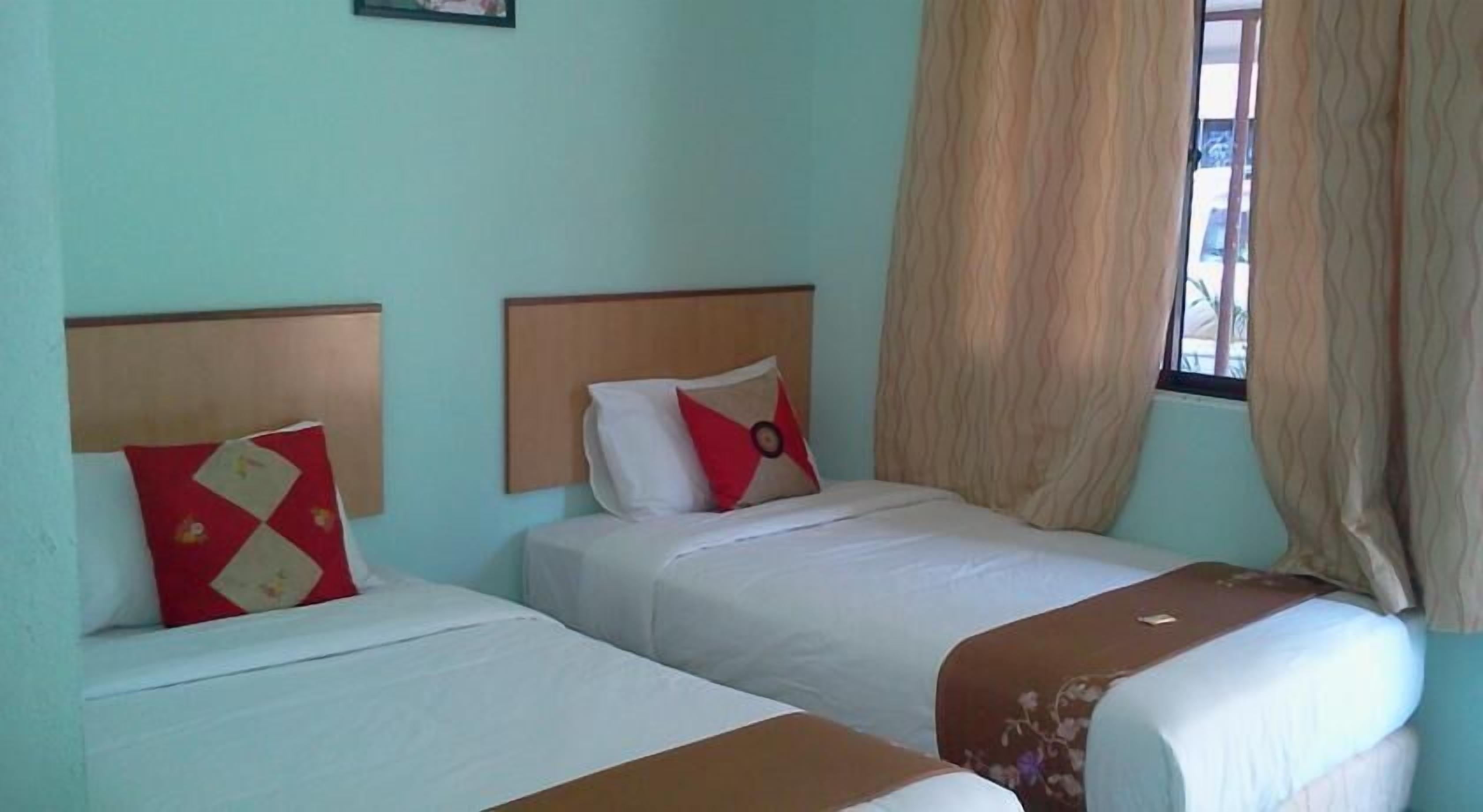 A room with two beds, each with a headboard, a window with curtains, and a small picture on the wall.