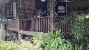 Um edifício de madeira com varanda, plantas em vasos e uma bicicleta.