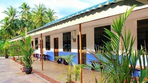 Um edifício de dois andares com varanda coberta, plantas em vasos e calçada de azulejos.