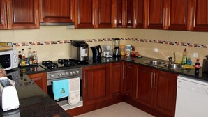 A kitchen with wooden cabinets, a stove, a microwave, a dishwasher, and various kitchen appliances. - Villa St Aubyn (São Vicente)