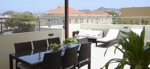 A rooftop terrace with a dining table, chairs, a sofa, and a potted plant.