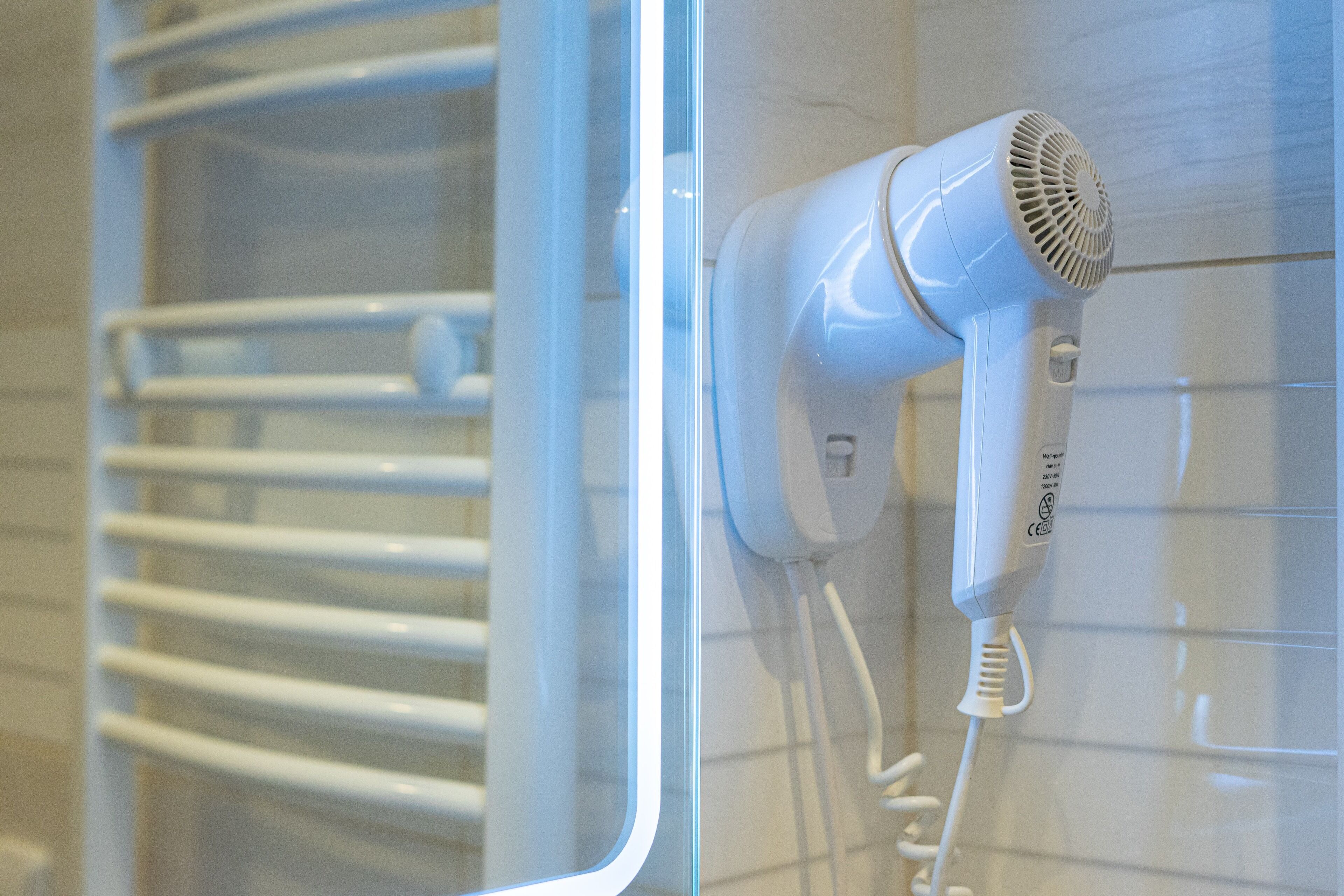 A white hair dryer mounted on a wall with a clear glass shower enclosure.