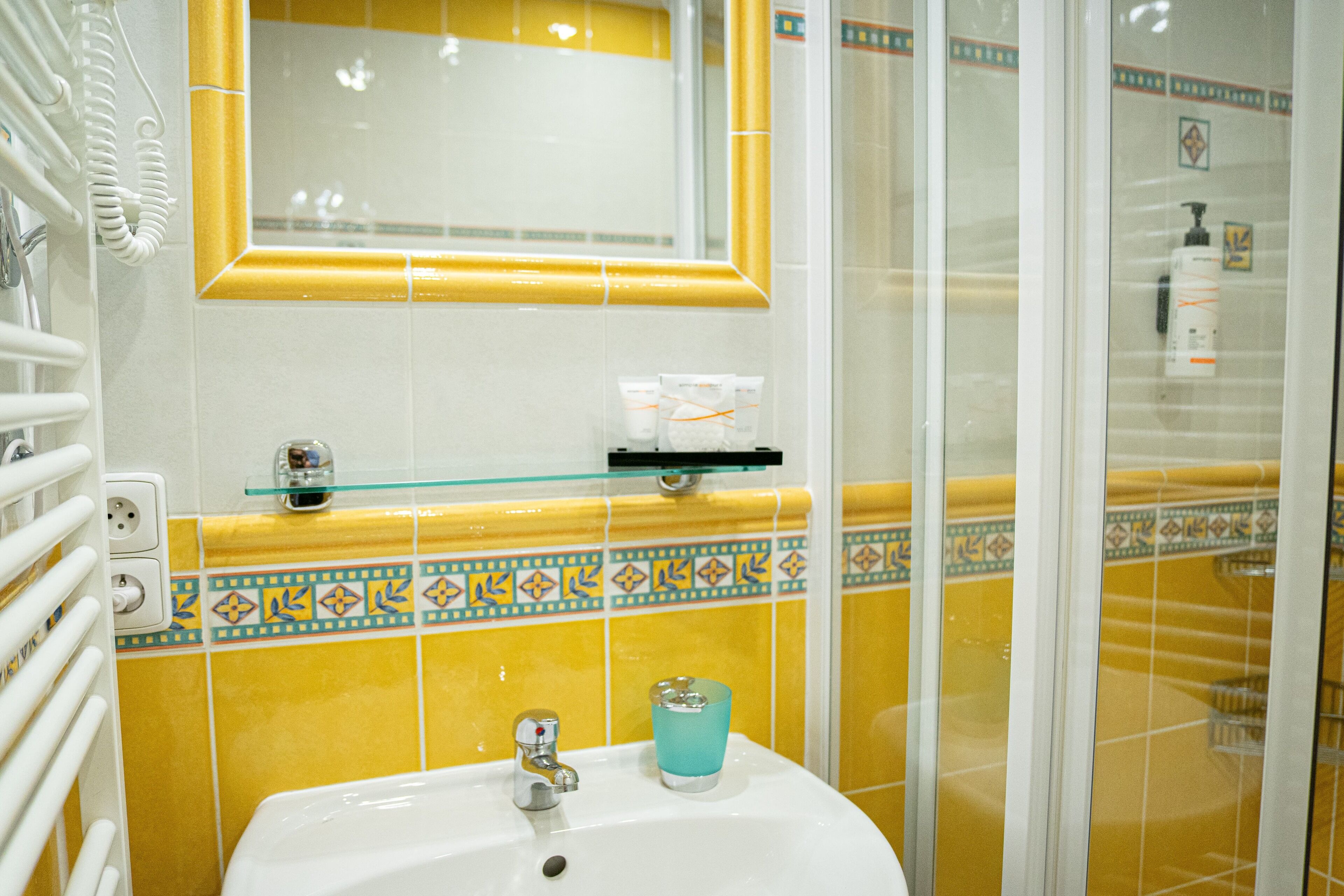A bathroom with a yellow tiled wall, a white sink, and a glass shower enclosure.