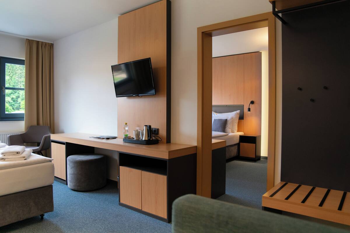Ein Hotelzimmer mit Bett, Schreibtisch, Flachbildfernseher, Stuhl, einem kleinen Hocker und einem Kleiderschrank.