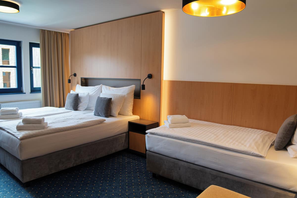 Ein Hotelzimmer mit zwei Betten, einem Holzkopfteil, einem Nachttisch und einem Fenster mit Vorhängen.