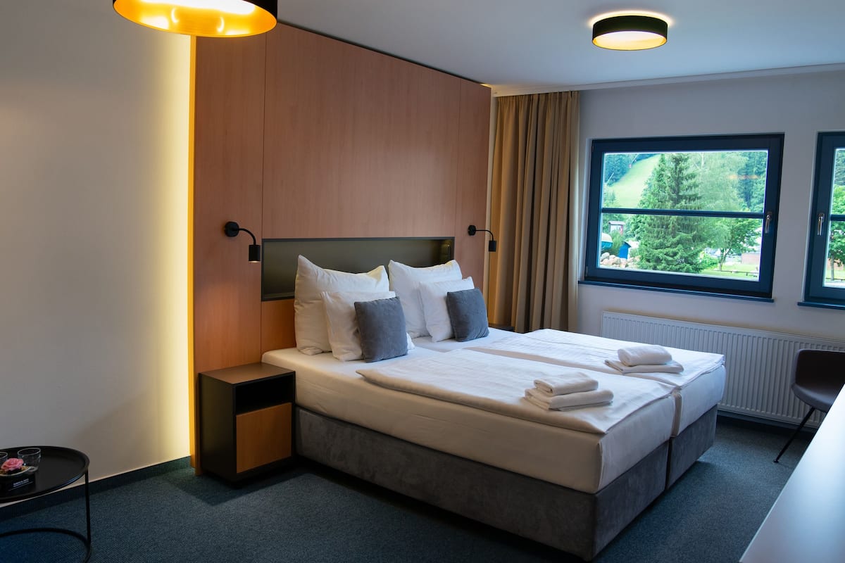 Ein modernes Hotelzimmer mit einem großen Bett, Nachttischen, einem Fenster mit Blick auf Grünflächen und einer Deckenleuchte.