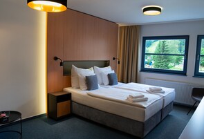 Una habitación de hotel moderna con una cama grande, mesitas de noche, una ventana con vistas a zonas verdes y un candelabro.
