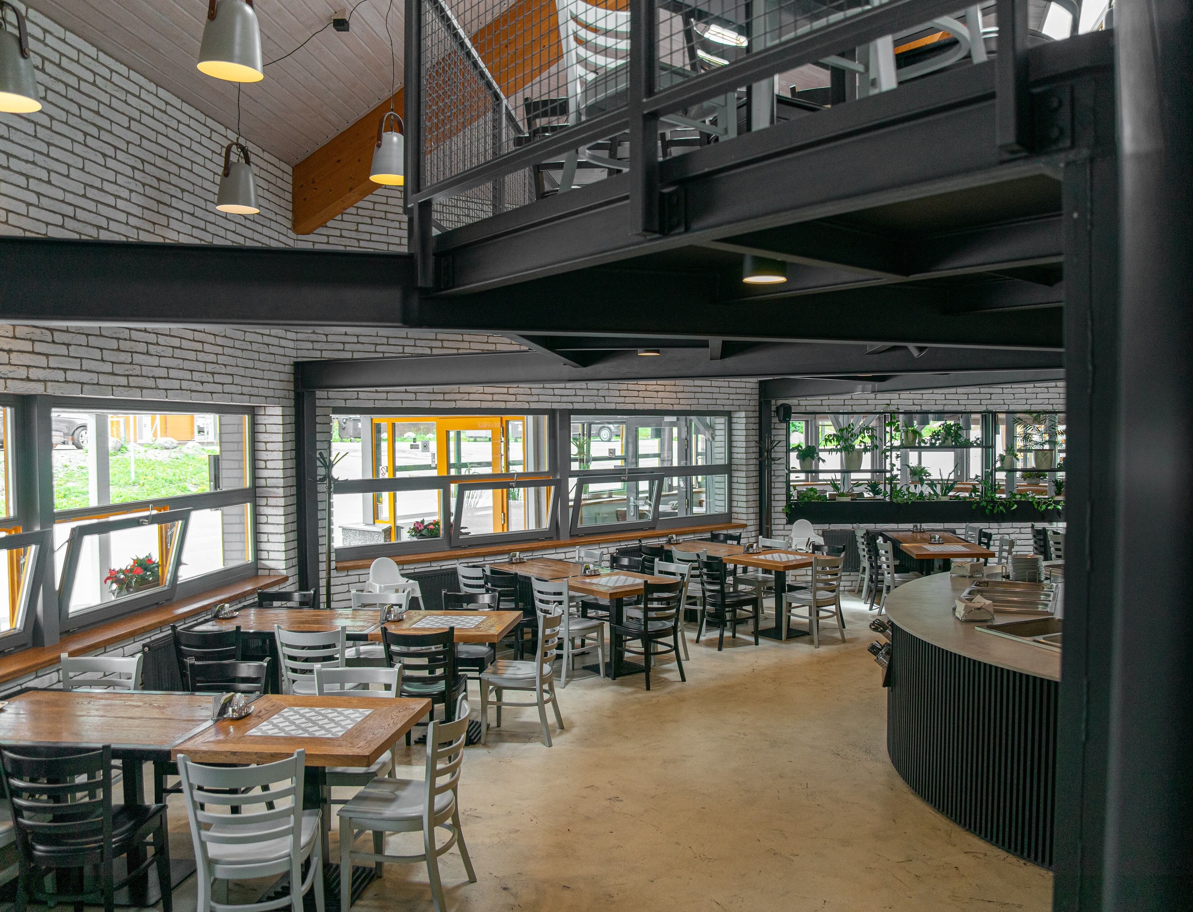 A spacious restaurant with high ceilings, exposed brick walls, and large windows offering views of the outside.