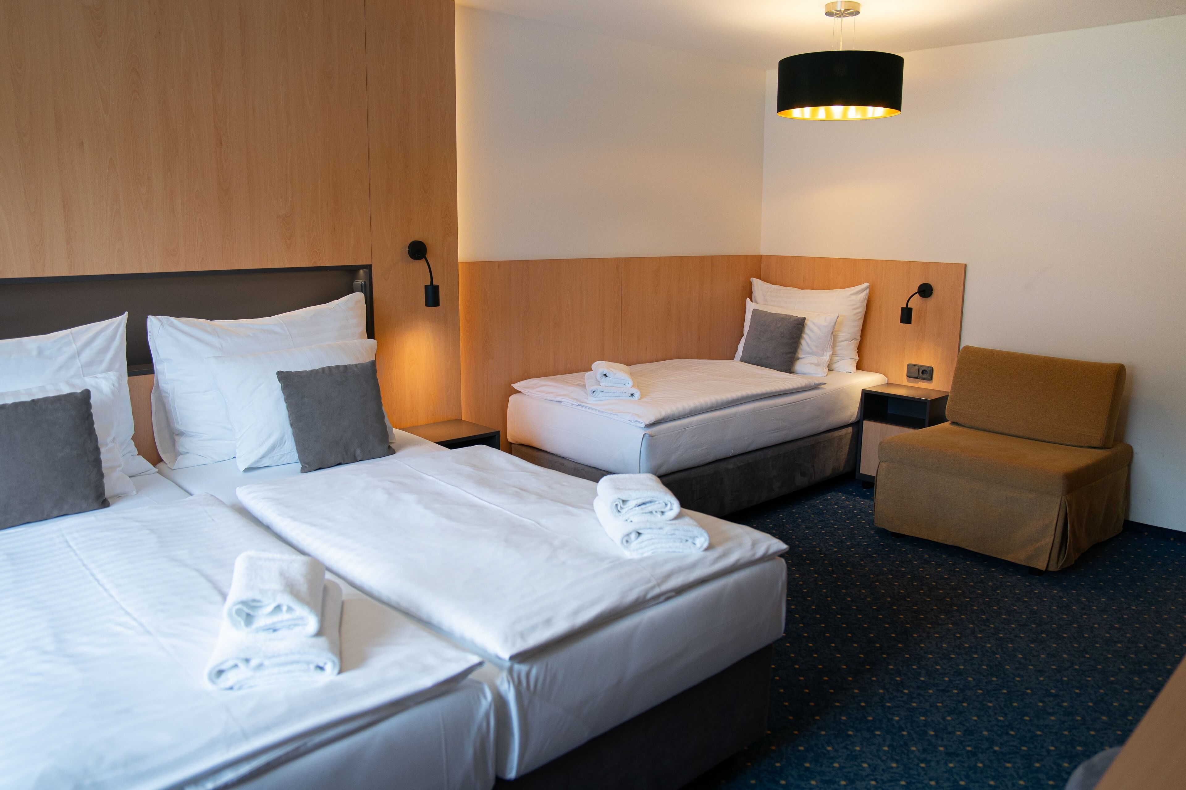 Habitación de hotel con dos camas, una mesita de noche, una silla y una lámpara fijada a la pared.