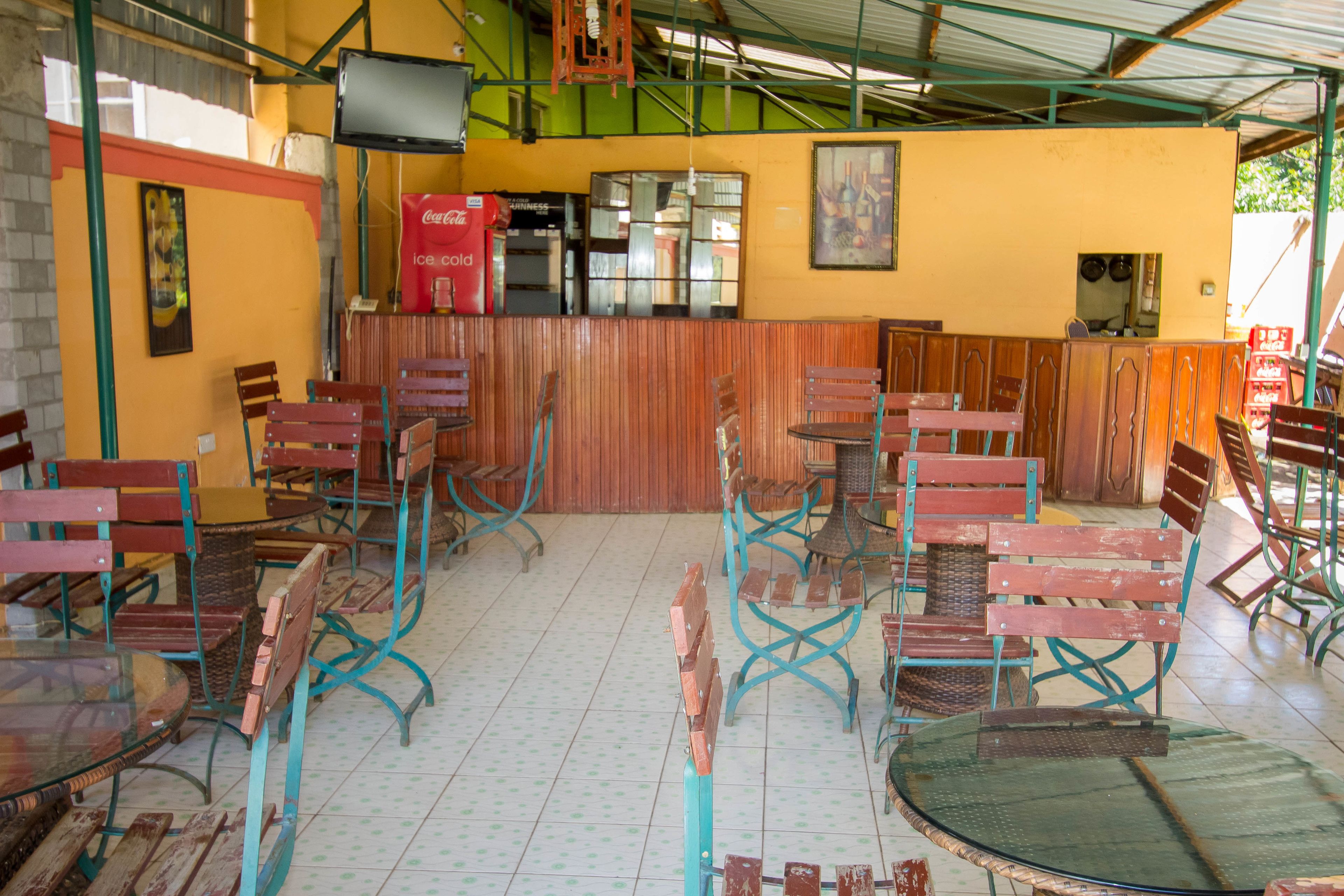 A restaurant with wooden and metal chairs, a counter with a Coca-Cola cooler, and a tiled floor.