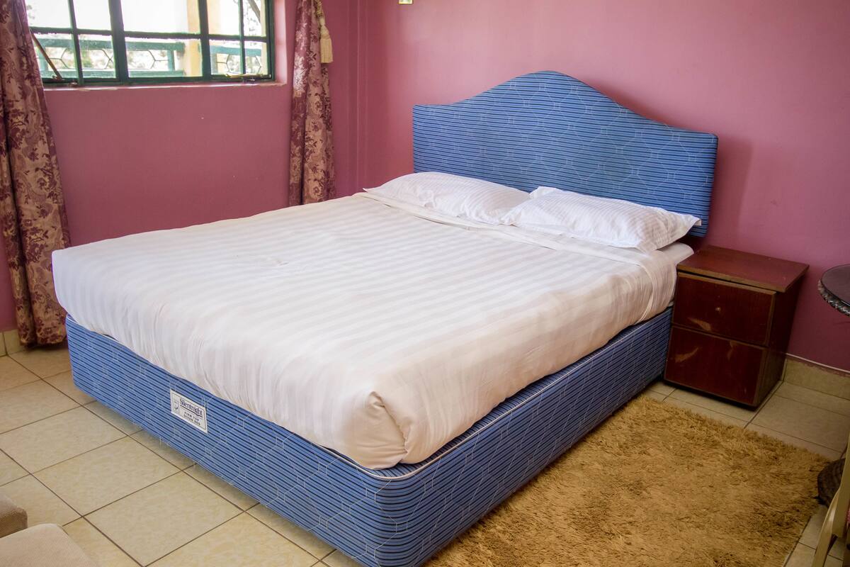 A bed with a blue headboard, a wooden nightstand, and a brown rug.