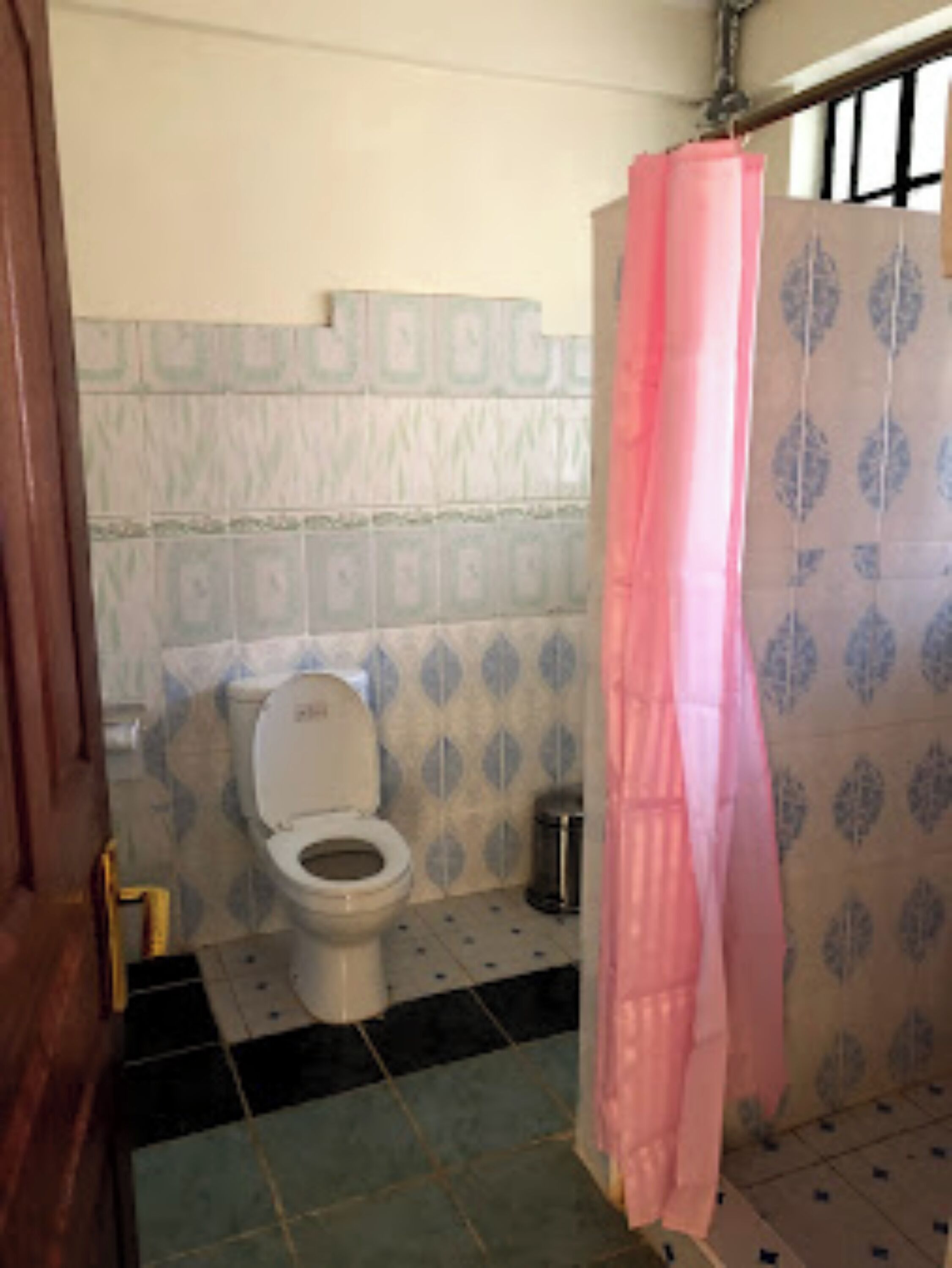 A bathroom with a toilet, a trash bin, and a shower curtain.