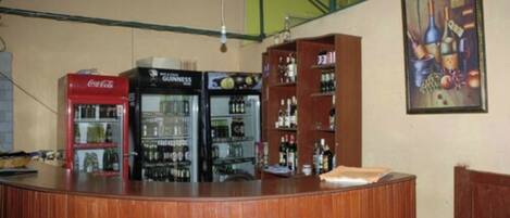 A bar area with a wooden counter, a Coca-Cola refrigerator, a Guinness refrigerator, and shelves with bottles.