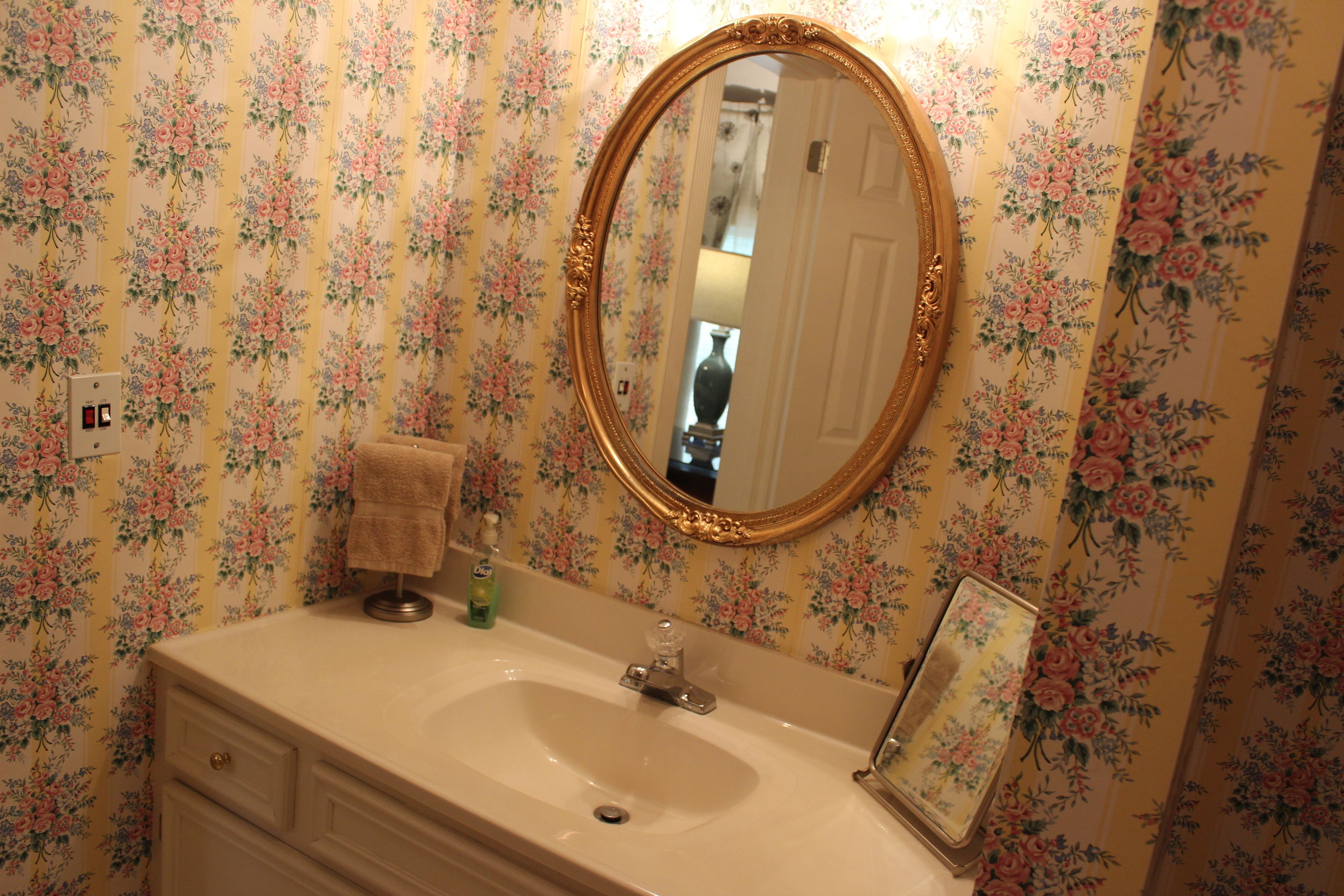 Un baño con papel tapiz floral, un lavamanos con espejo y una toalla sobre la encimera.