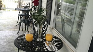 A round table with two chairs, a vase with a red rose, and two glasses of orange juice on a porch. - Huffman House (Minden)