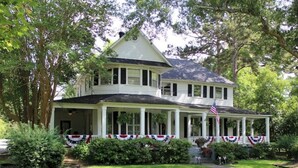 A two-story house with a porch, surrounded by trees and greenery. - Huffman House (Minden)