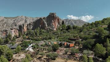 A mountainous landscape with a cluster of modern buildings, likely a resort or hotel, surrounded by dense greenery and rocky terrain.