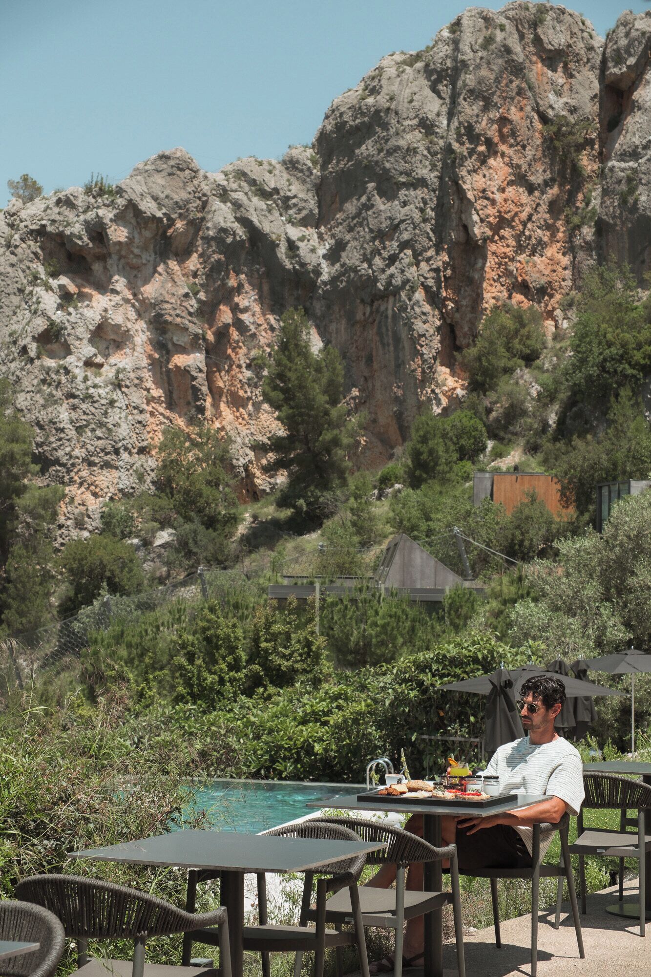 A person dining at an outdoor table with a view of rocky cliffs and greenery.