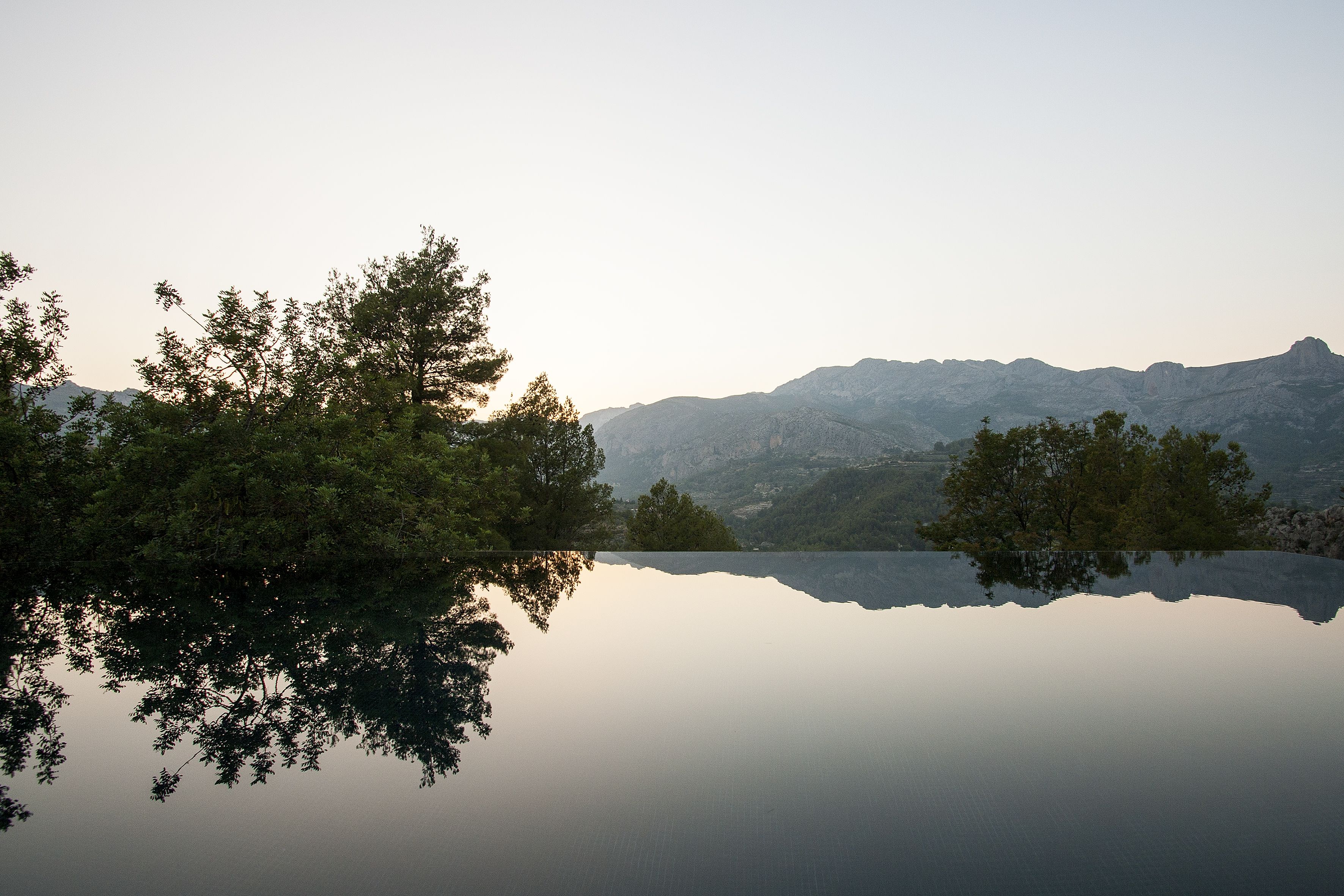 A calm lake reflecting trees and mountains.