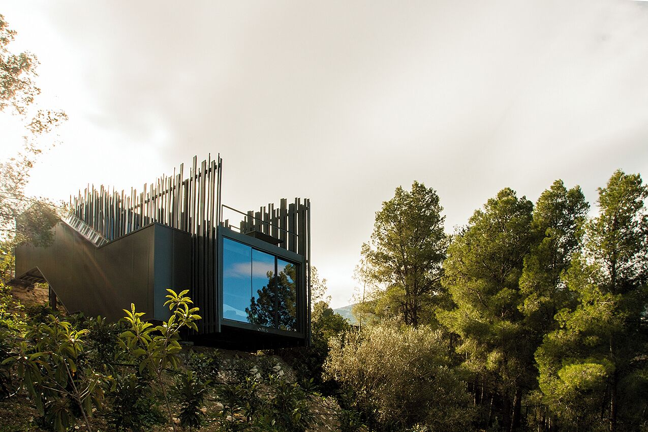 Un edificio moderno con un diseño exterior único, rodeado de abundante vegetación.