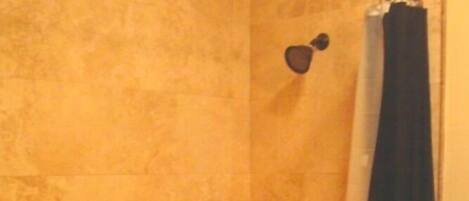 A shower with a tiled wall, a small shelf, and a shower curtain.