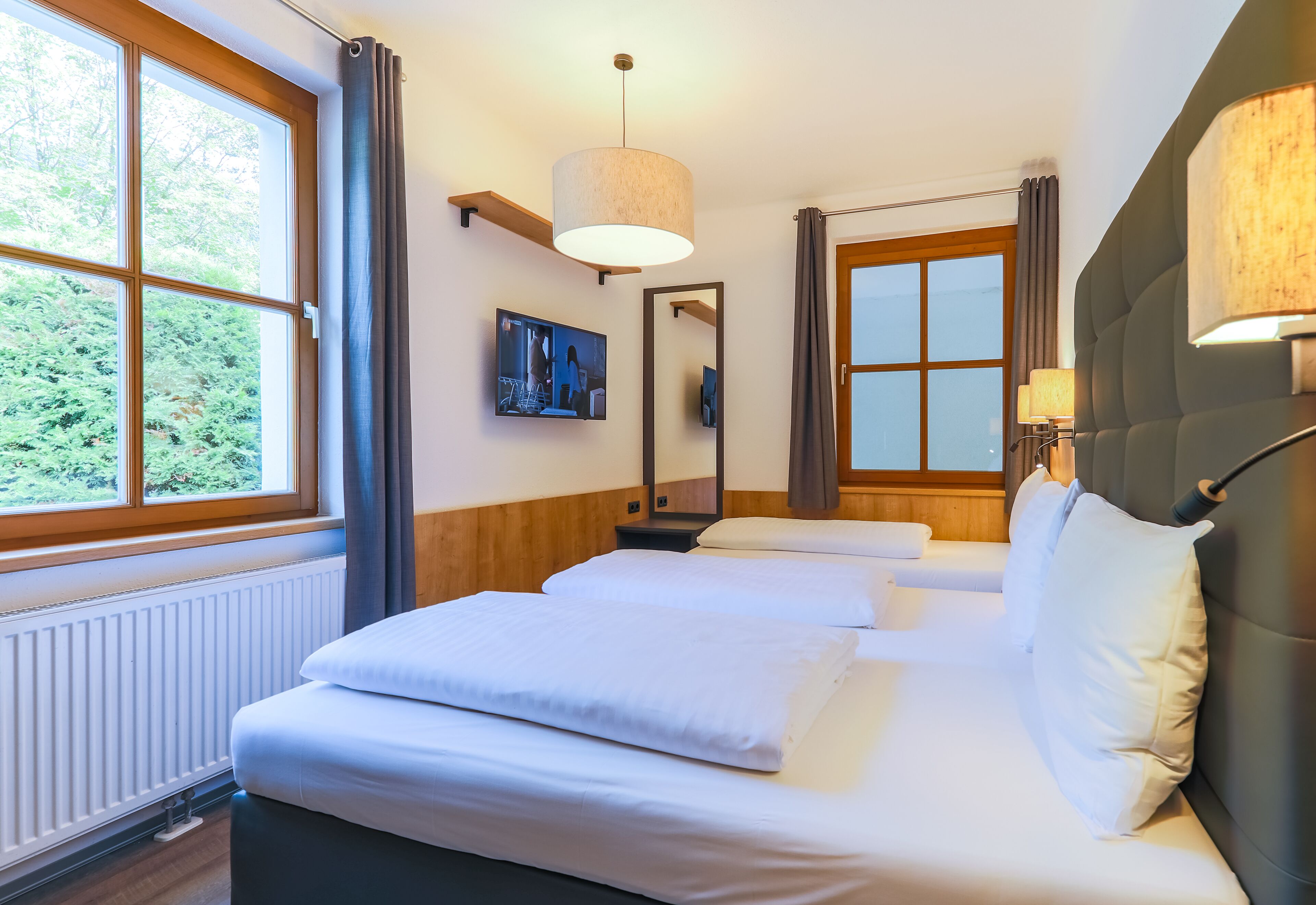 A hotel room with a large bed, a television, a mirror, and a window with curtains.