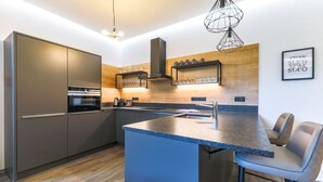 A modern kitchen with a central island, built-in appliances, and a wooden accent wall. - Kitz Residenz by Alpin Rentals - incl Summercard (Kaprun)