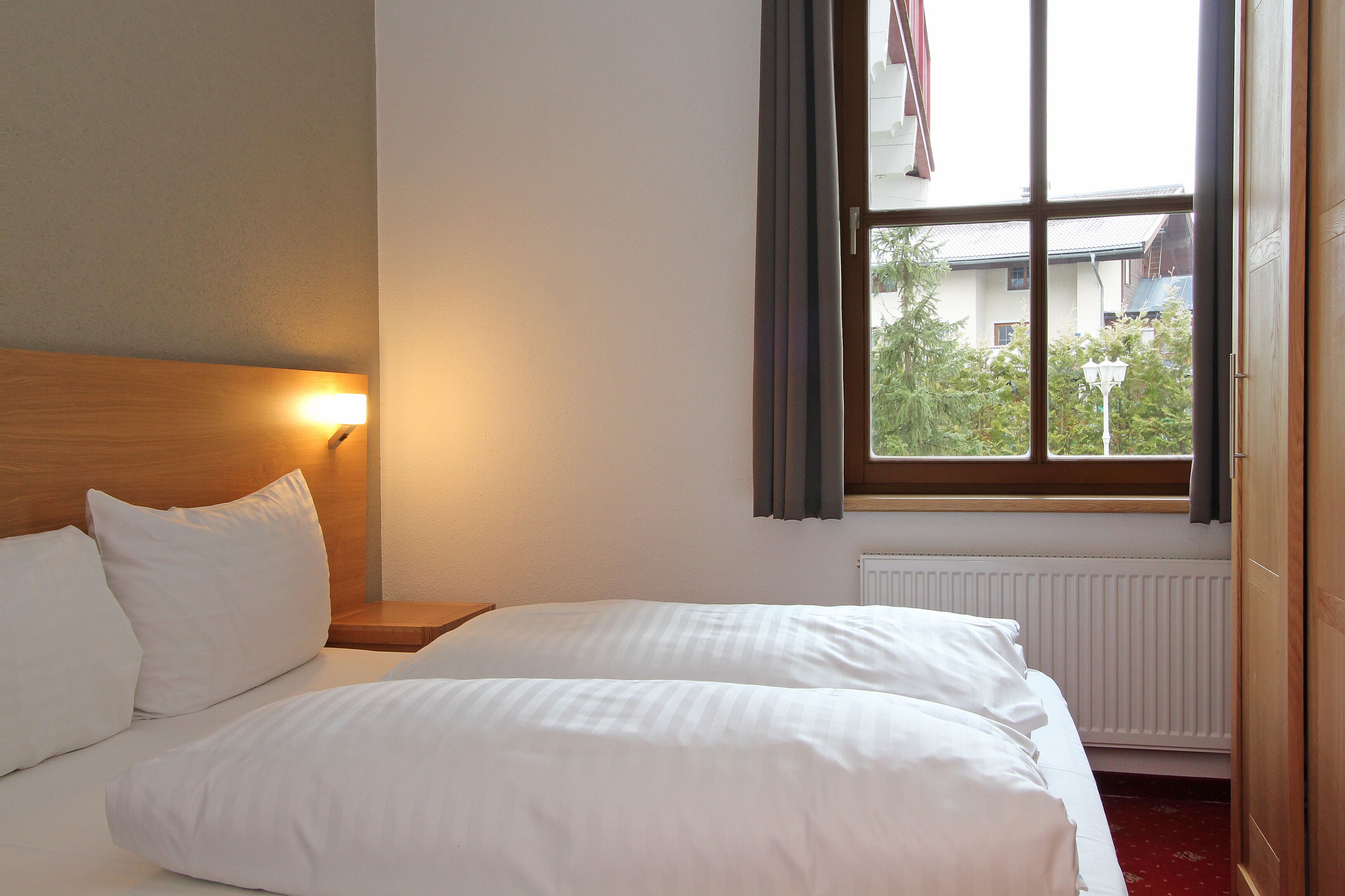 Una habitación de hotel con dos camas, una mesita de noche, una ventana con cortinas y un radiador.