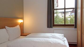 Una habitación de hotel con dos camas, una mesita de noche, una ventana con cortinas y un radiador.